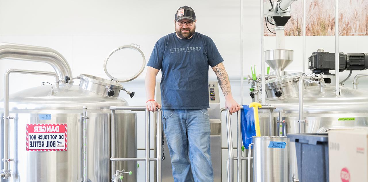 Sean Johnson standing in the brewing laboratory beside steel kettles.