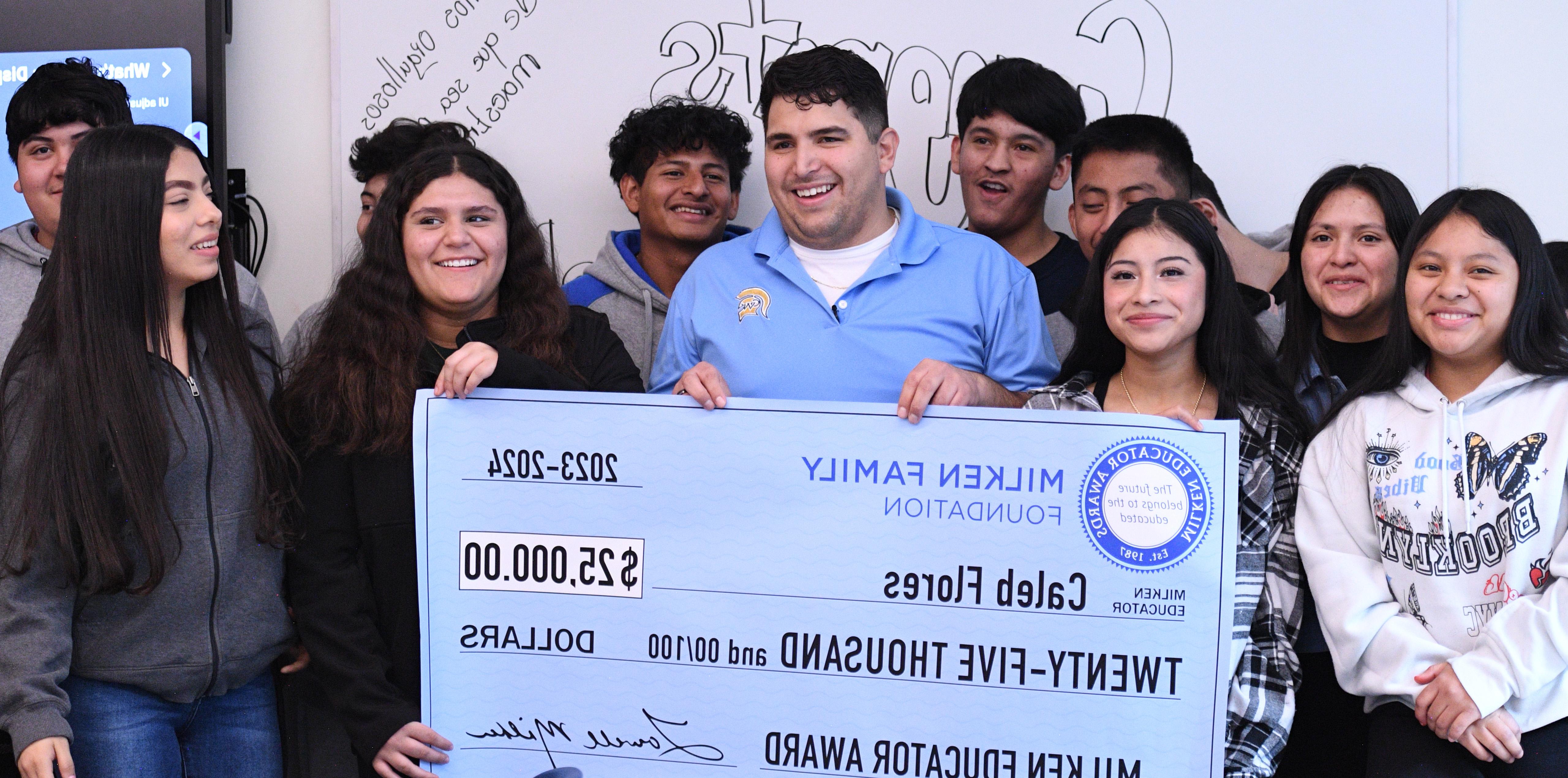 Caleb Flores holding up a big check with his students standing behind him