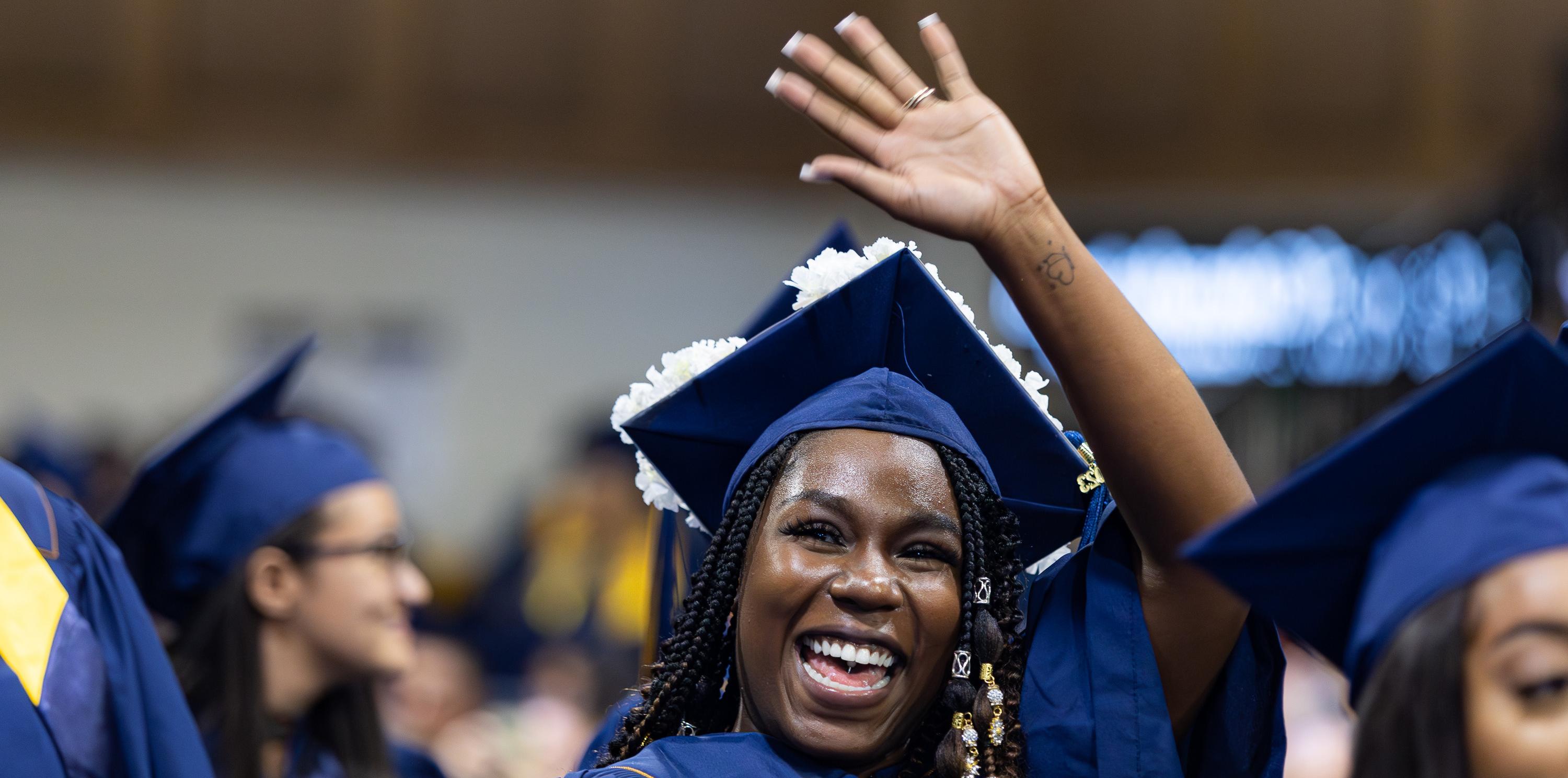 毕业典礼上戴着学士帽、穿着学士服的女大学生，微笑着挥手