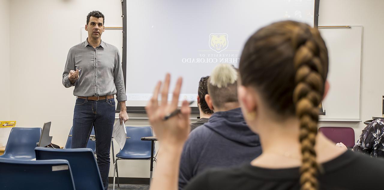一个年轻的大学生在教室里举手，老师站在前面.