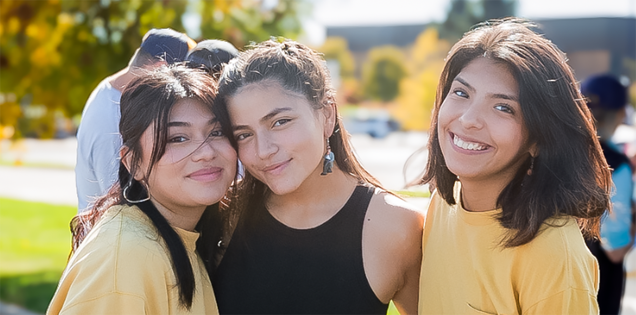 在一场庆祝拉美裔/拉丁裔社区的活动中，三个大学生微笑着站在一起。