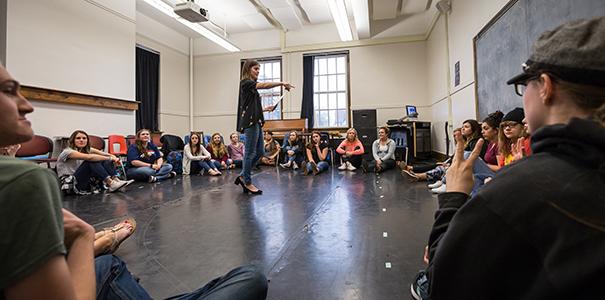 instructor st和ing in circle of students in a large room conducting acting class